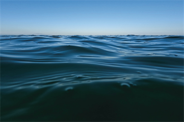 Water at the beach, the camera is half-submerged. The sky is blue and the water is a dark green.